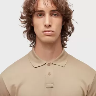 Homem com polo bege de algodão e dois botões em fundo branco.