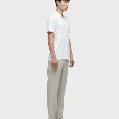 Homem de pé com camisa polo branca, calças bege e sandálias pretas