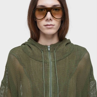 Pessoa a usar óculos de sol com armação castanha e peça de vestuário verde em malha aberta