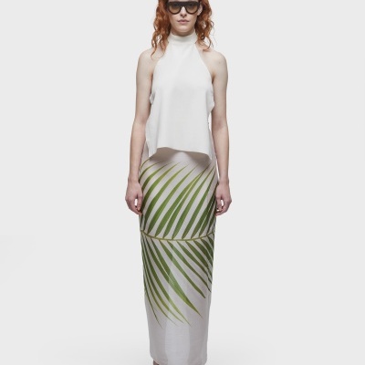 Vestido feminino longo branco com estampa de folhas verdes, modelo com óculos escuros e sandálias pretas em fundo branco