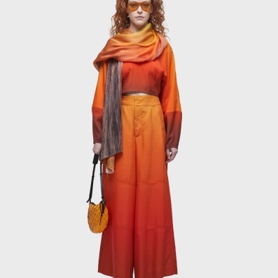 Mulher com roupa laranja e vermelha, lenço amarelo, óculos escuros e bolsa amarela