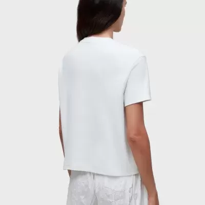 Mulher vista de costas com camisola branca de manga curta e calças brancas enrugadas