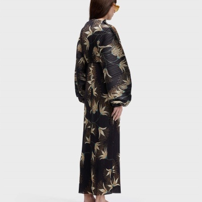 Mulher de perfil usando vestido comprido plissado com padrão floral preto e sandálias castanhas