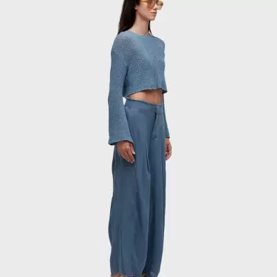 Mulher com camisa de malha azul, calças largas azuis, sandálias e óculos de sol amarelos