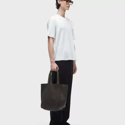 Homem com camiseta branca, calças pretas e mala de couro preta