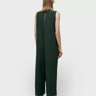 Macacão verde escuro sem mangas usado por trás, com sandálias marrons e sola branca.