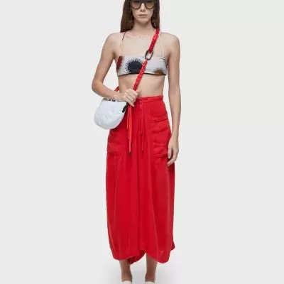 Mulher com top curto, saia vermelha, sapatos brancos e bolsa branca com alça vermelha