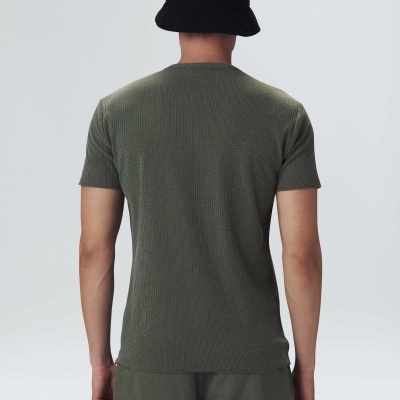 Homem de costas vestindo camisola verde de manga curta, calças cargo verdes e chapéu preto