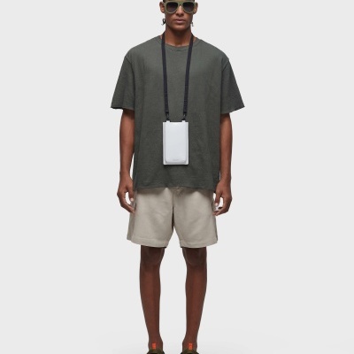 Homem com t-shirt verde, calções beges, óculos escuros e bolsa branca pendurada no pescoço