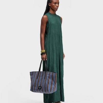 Mulher de vestido verde escuro e bolsa às riscas azuis e castanhas