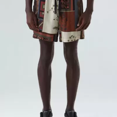 Calções com padrão de quadrados e estampas florais em várias cores, usados por homem com sapatos e t-shirt pretos