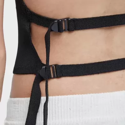 Detalhe da parte de trás de roupa preta com tiras e fivelas, calças brancas caneladas