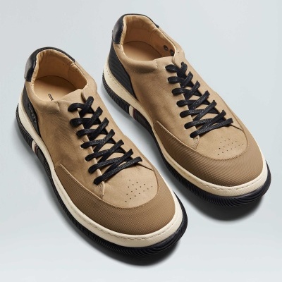 Sapatilhas camel com sola branca e preta, cadarços pretos, fundo cinzento