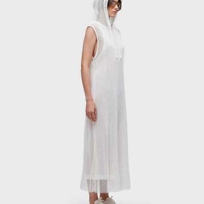 Mulher com vestido comprido branco de malha transparente com capuz, ténis brancos e óculos de sol
