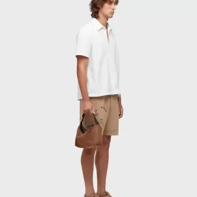 Homem com camisa branca, calções bege, sandálias castanhas e mala castanha