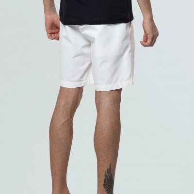 Homem visto de costas com calções brancos, t-shirt preta e sapatos pretos em fundo cinza.