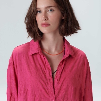 Camisa rosa de tecido com textura ligeiramente vincada e colar laranja.