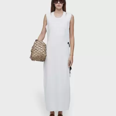 mulher com vestido branco comprido a segurar mala bege com padrão de escamas
