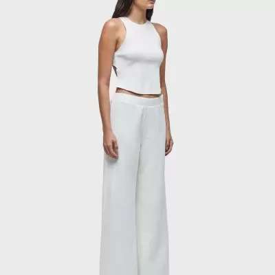 Mulher com top branco, calças largas brancas, óculos de sol e sandálias pretas