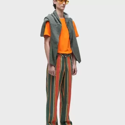 Homem com t-shirt laranja, calças riscas verticais e casaco cinza nos ombros