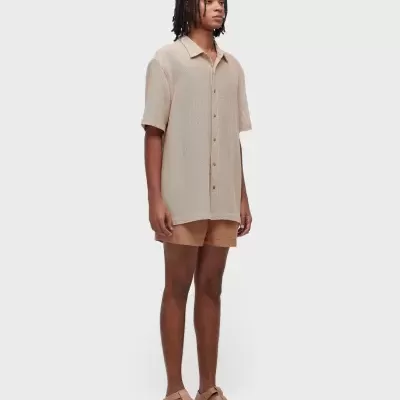 Homem com camisa bege, calções castanhos claros e sandálias bege