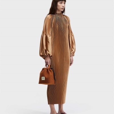Pessoa com vestido midi plissado cor camel segurando mala castanha de pelúcia com etiqueta