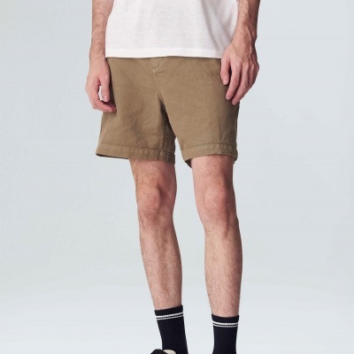 Homem com calções marrons, t-shirt branca, meias pretas riscas brancas e sapatilhas bege em fundo branco