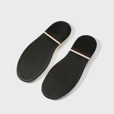 Solas de sapato pretas com detalhes em vermelho e branco sobre fundo cinzento claro