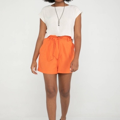 Mulher com t-shirt branca, calções laranja com faixa e sandálias castanhas em fundo branco