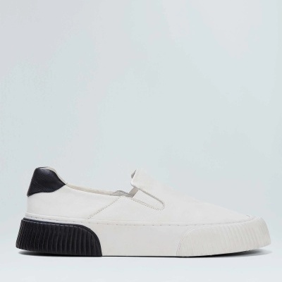 Tênis slip-on branco com sola preta texturizada em fundo cinza