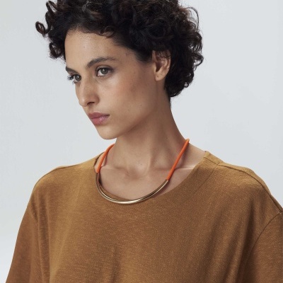 Mulher com t-shirt castanha e colar metálico com cordão laranja