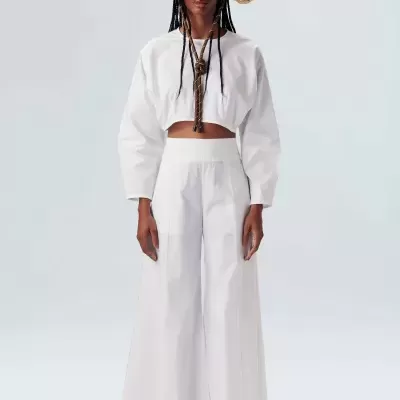Mulher com conjunto branco cropped e calças largas, chapéu de palha e colar