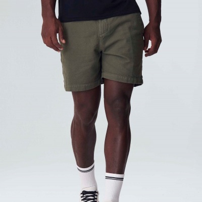 Homem a vestir calções verdes, t-shirt preta, meias brancas riscas pretas e ténis brancos com atacadores pretos