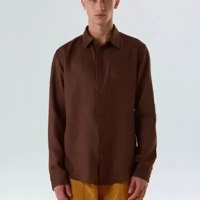 Homem com camisa castanha e calças amarelas em fundo branco