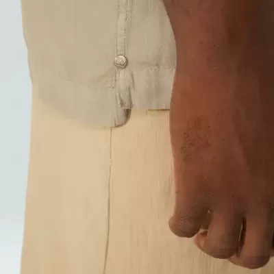Detalhe de roupa bege com botão prateado e mão ao lado