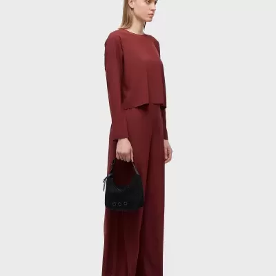 Mulher com conjunto vinho blusa e calças largas, bolsa preta e sapatos pretos com detalhes verdes