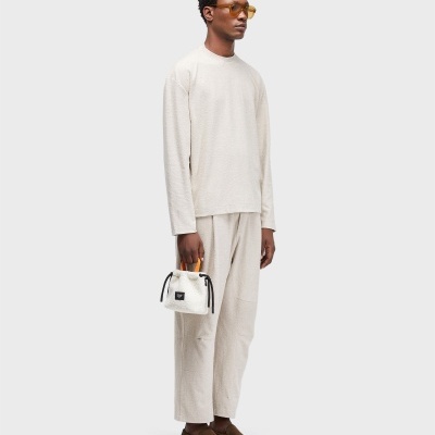 Homem com camisola e calças creme, mala branca, sapatos castanhos e óculos de sol amarelos
