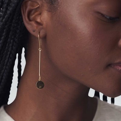 Brinco pendente dourado em orelha de pessoa com cabelo trançado