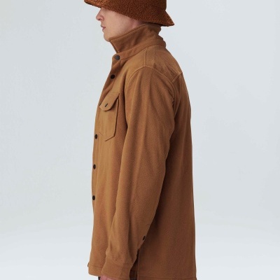 Homem de perfil com camisa fleece castanha, calças quadriculadas escuras e chapéu bucket castanho