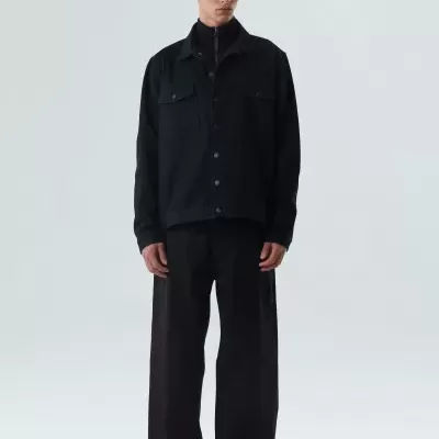 Homem vestido com camisa preta de botões e calças largas pretas