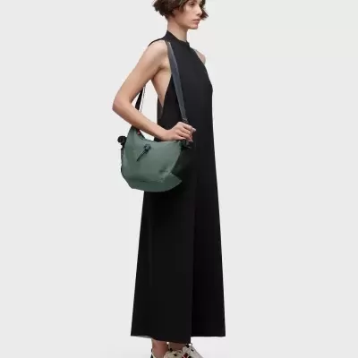 Mulher com vestido preto longo e bolsa verde escura ao ombro