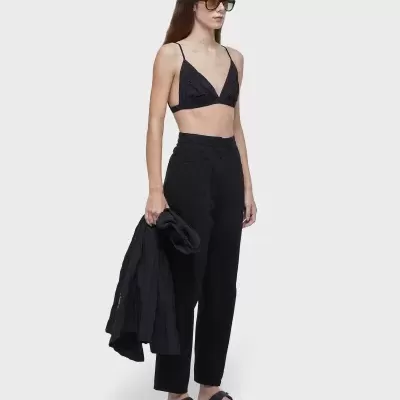 Modelo feminina com roupa preta casual incluindo top de alças, calças e sandálias, segurando um casaco