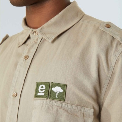 Camisa bege de algodão com botões, patches verdes com letra e imagem de árvore