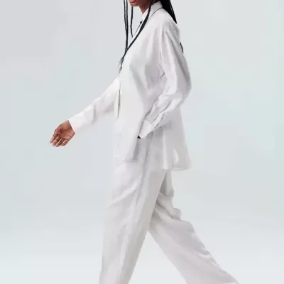 Mulher a caminhar com fato branco e sandálias castanhas em fundo claro