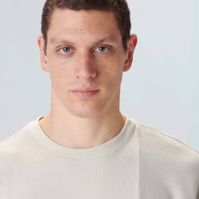 Homem com camisola creme em fundo cinza claro