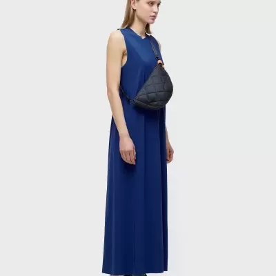Mulher com vestido azul longo, saco preto acolchoado e ténis pretos com detalhes verdes.