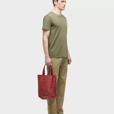 Homem com roupa casual verde e bege a segurar uma tote bag vermelha com textura textil.