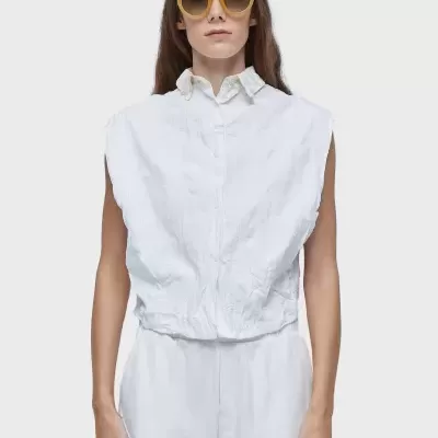 modelo veste colete branco, camisa branca, calções brancos e óculos de sol amarelo-alaranjados