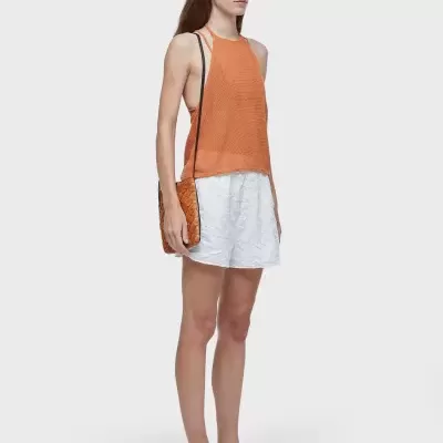 Mulher com top laranja, calções brancos, óculos de sol e sandálias pretas