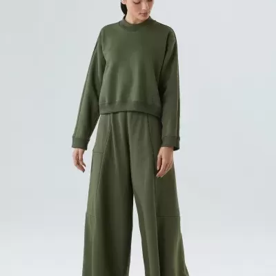 Conjunto de roupa verde-oliva com camisola e calças largas em fundo cinzento.